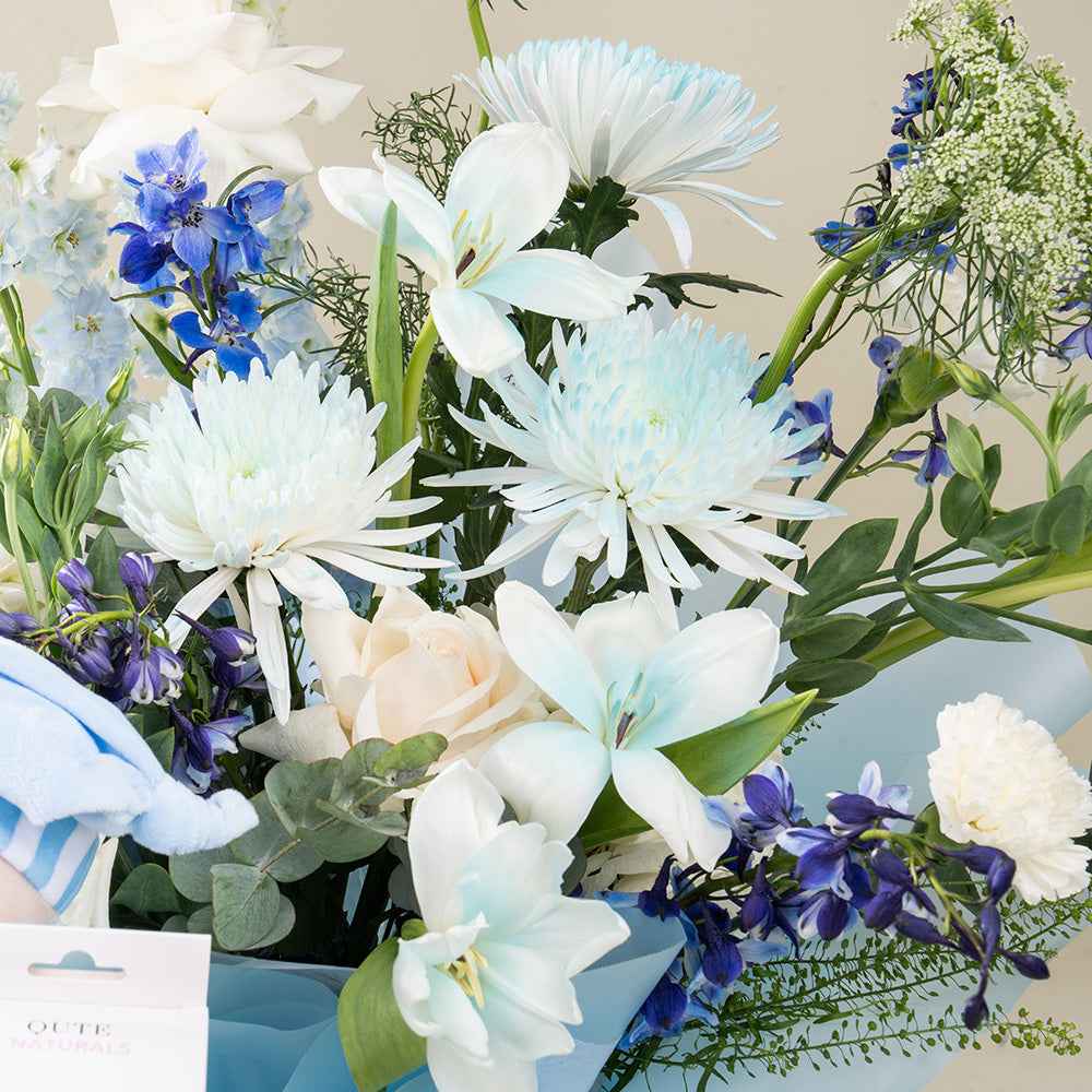Qute x Plaza Hollandi luxury fresh blue and white flower bouquet with delphiniums, roses, and chrysanthemums wrapped in soft blue paper for fresh flower delivery in Doha Qatar