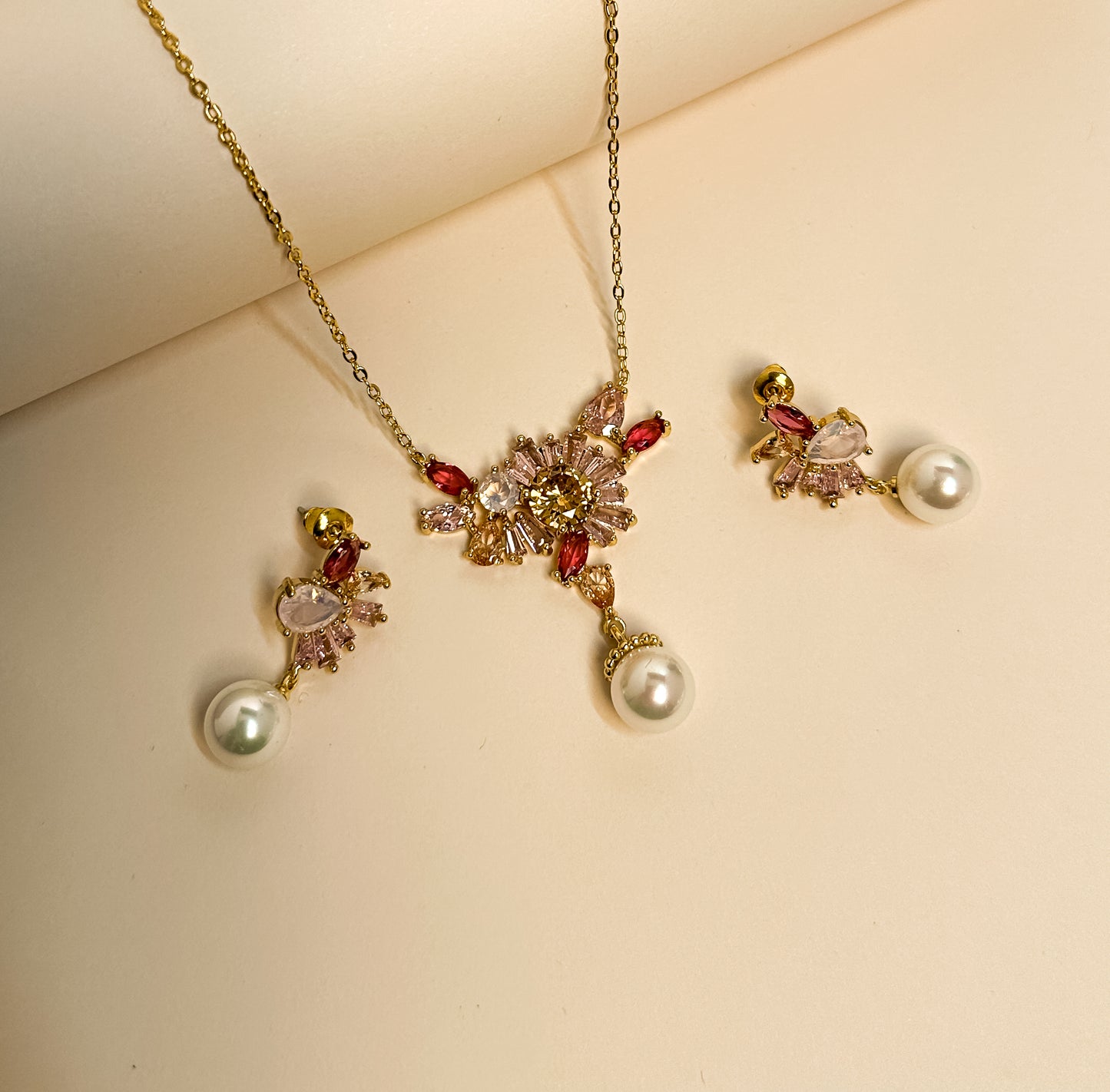 Elara jewelry set displayed on deep maroon velvet featuring a gold chain necklace with a floral crystal cluster pendant in shades of pink, yellow, and clear stones with a hanging white pearl drop, and matching screw-back earrings with crystal clusters and pearl drops in Doha Qatar