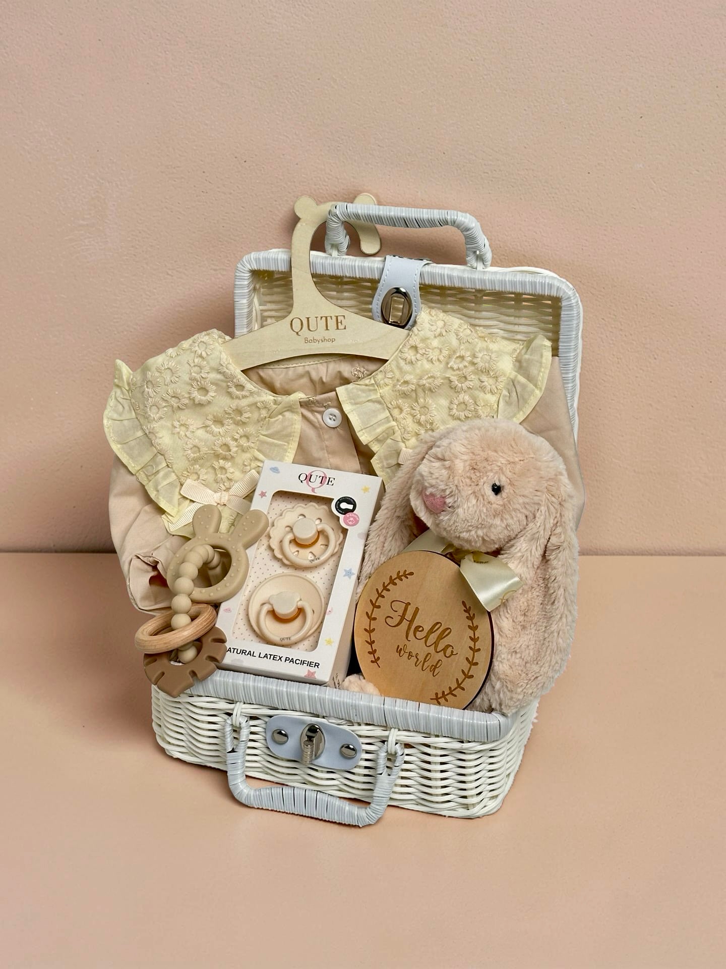 Deluxe yellow baby girl gift set in white woven suitcase hamper with lace floral collar dress, plush bunny toy, Qute natural latex pacifiers, silicone bunny teether ring, and wooden milestone disc by Qute Gifts Doha Qatar