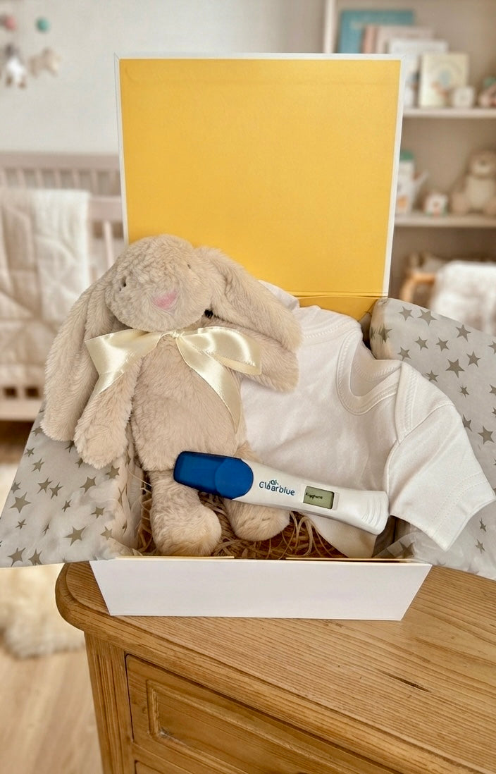 Pregnancy announcement gift box for husband featuring white onesie printed with Guess What Daddy Round Two, plush bunny toy, and Our Family Is Growing reveal card by Qute Gifts Doha Qatar