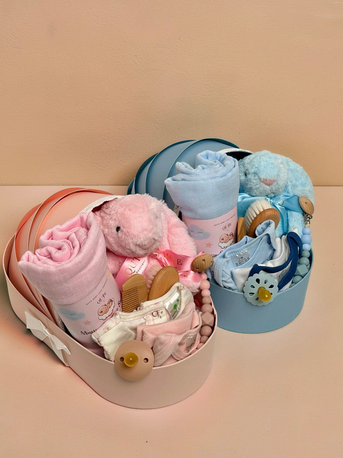 Luxury baby girl newborn gift hamper in a cradle-shaped pink box by Qute Qatar, featuring a pink swaddle, plush bunny, baby clothes, and wooden accessories for delivery in Doha.