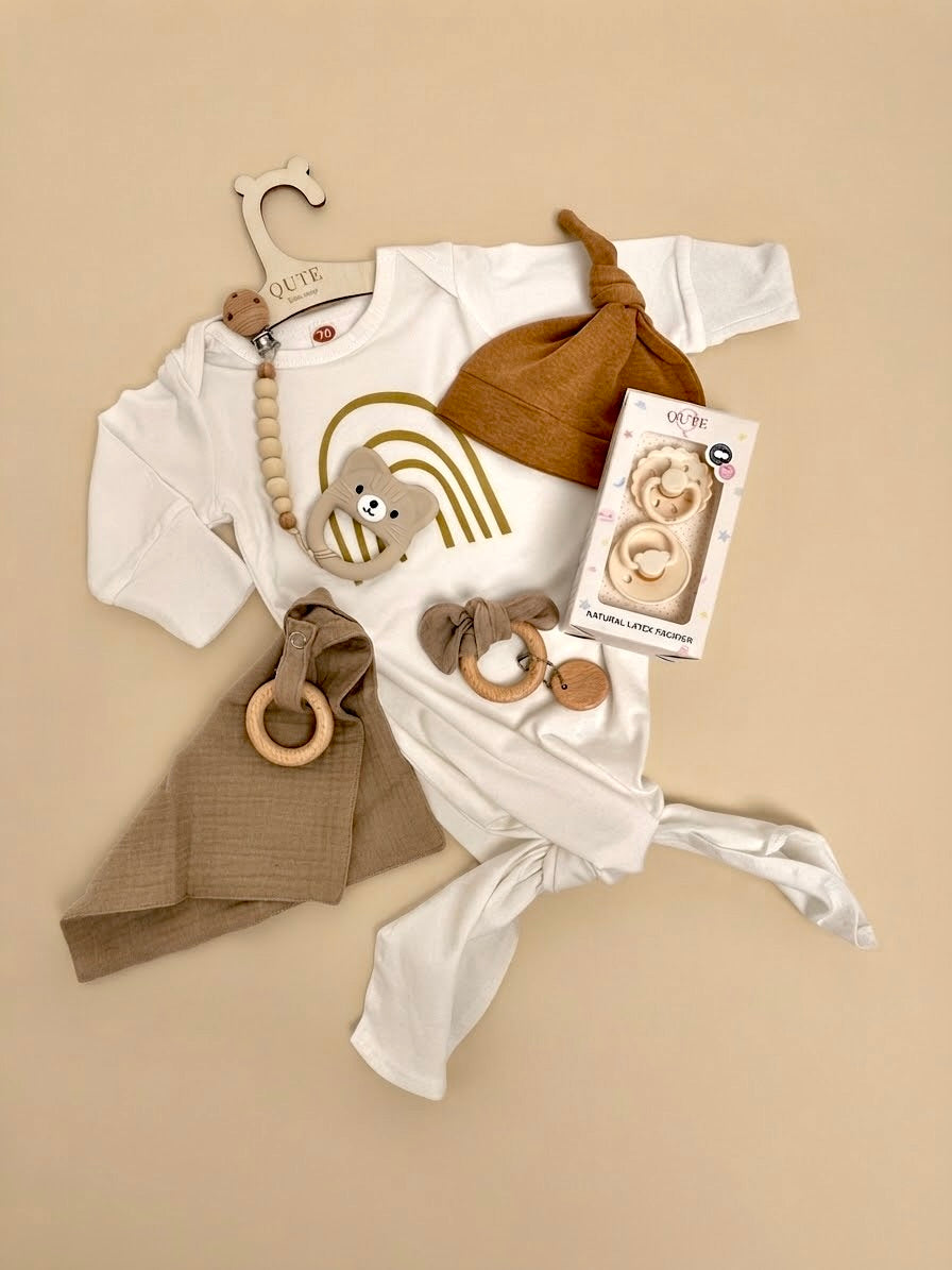 Luxury newborn baby gift set in a white keepsake suitcase by Qute Qatar, featuring a 3-6 months caramel outfit, bear teether, natural latex pacifiers, and wooden accessories for delivery in Doha.