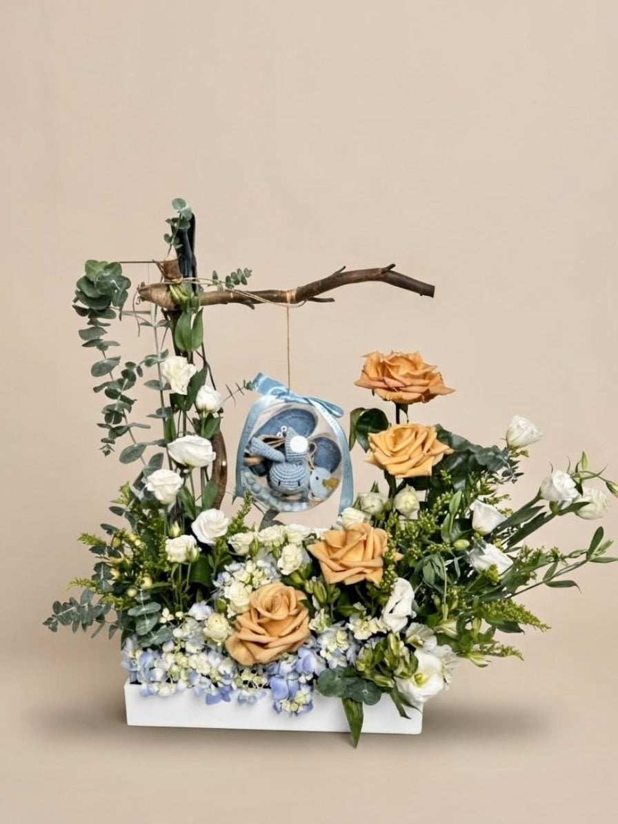 Baby Bloom Bubble newborn boy flower arrangement featuring champagne roses, blue hydrangeas, and an acrylic keepsake bubble with a blue crochet bunny rattle and custom name clip.