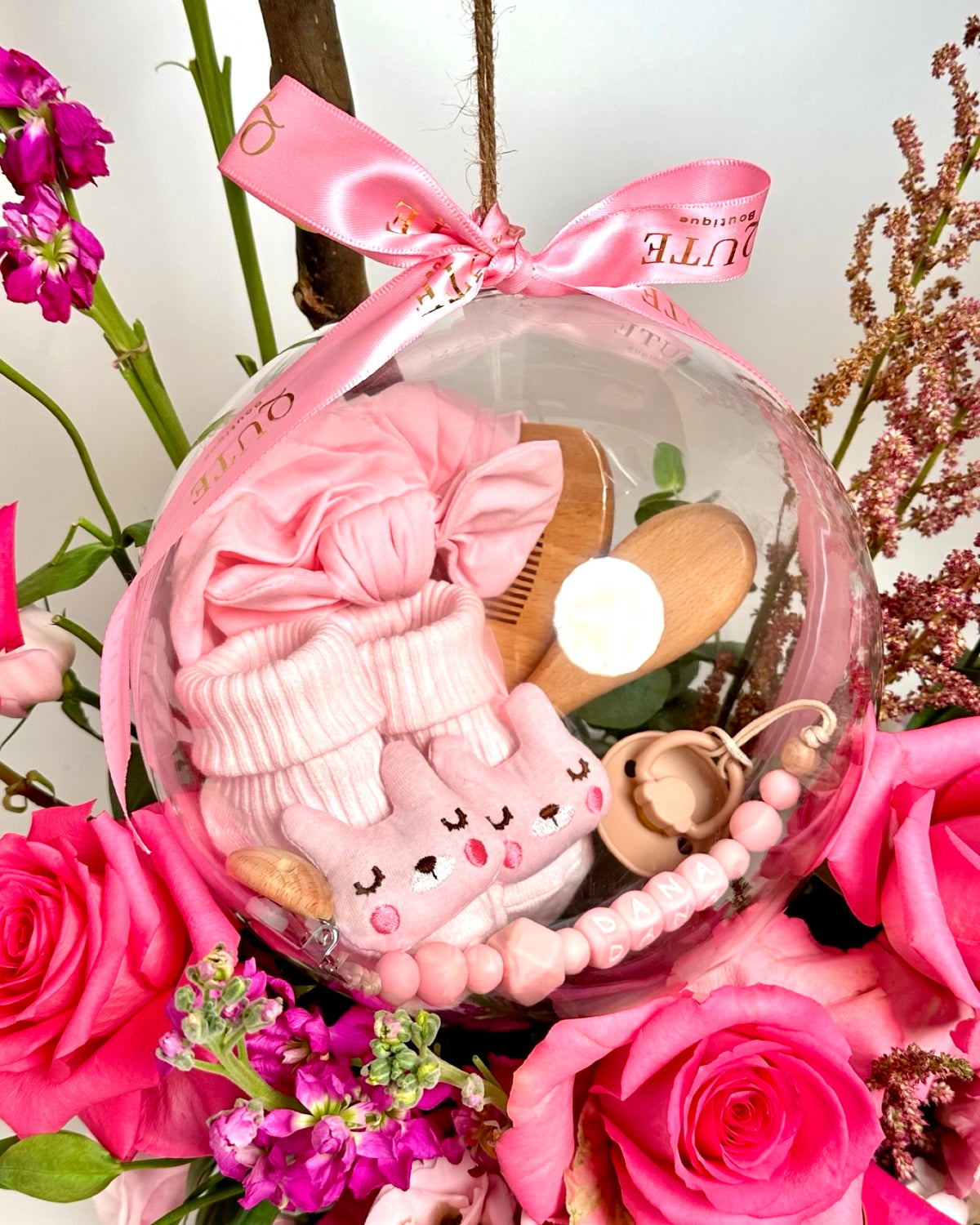 Same-day baby girl gift box featuring luxury pink roses and an acrylic keepsake bubble packed with practical newborn accessories for welcoming a new baby.