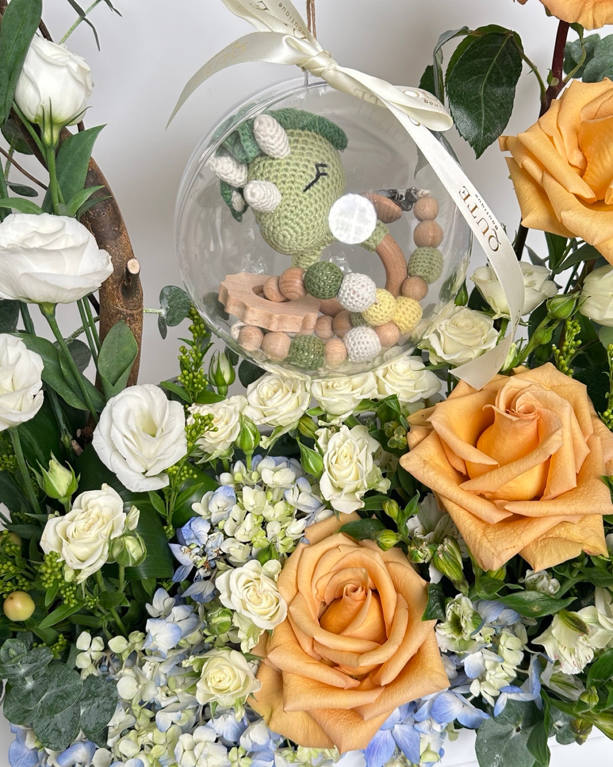 Champagne rose and blue hydrangea box arrangement with a hanging acrylic keepsake bubble enclosing a dinosaur toy and wooden accessories, styled by Plaza Hollandi.