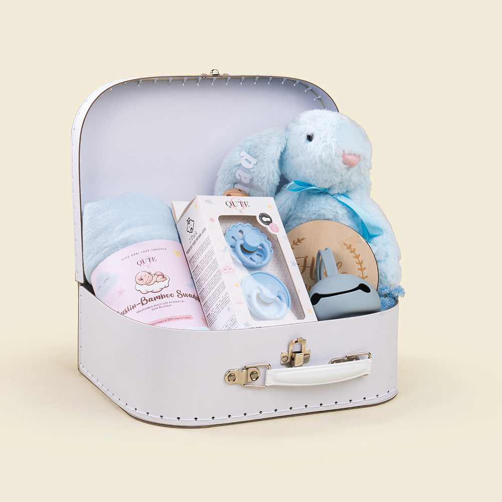 Plaza Hollandi x Qute luxury baby boy gift set in white vintage keepsake suitcase with plush blue bunny, bamboo swaddle blanket, pacifiers, and wooden milestone plaque for baby boy gifts in Doha Qatar