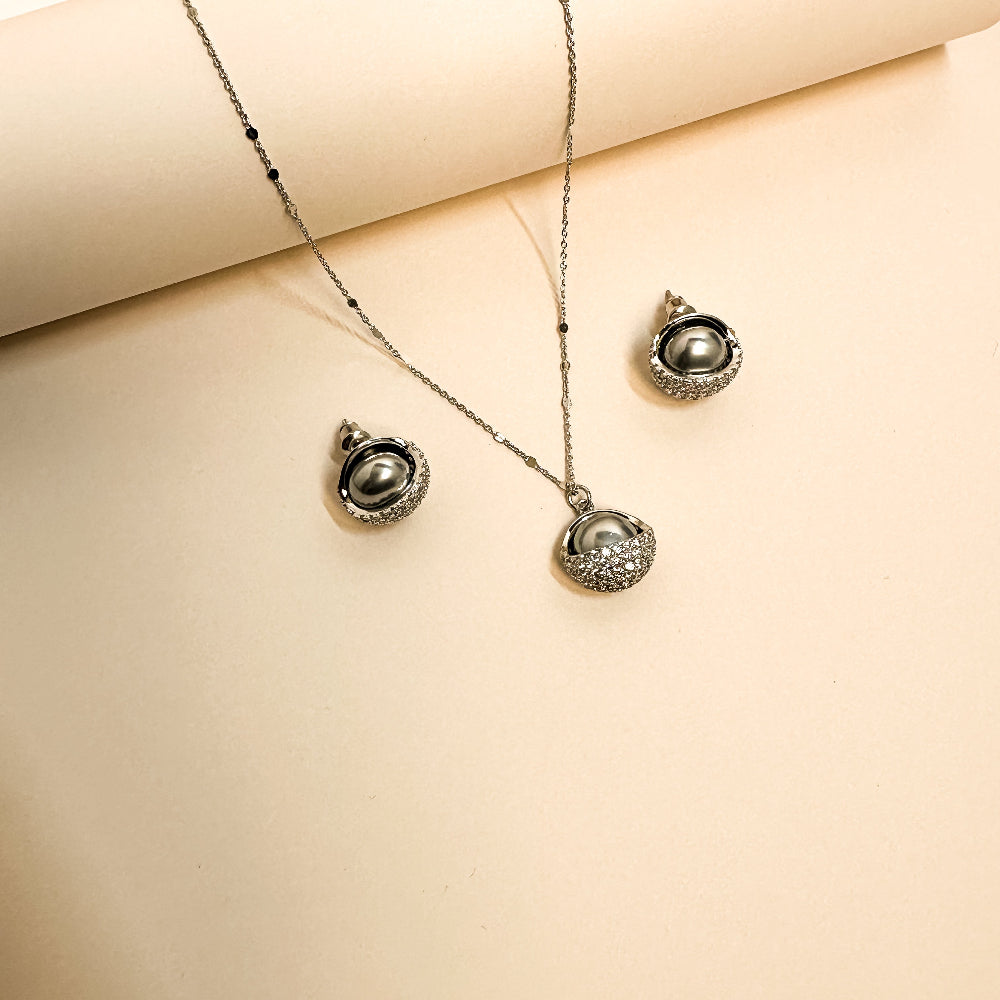 Elara jewelry set displayed on deep dark velvet featuring a silver chain necklace with a luminous dark pearl cradled in a sparkling pave-encrusted semi-circle cup, and matching stud earrings with dark pearls and pave details in Doha Qatar
