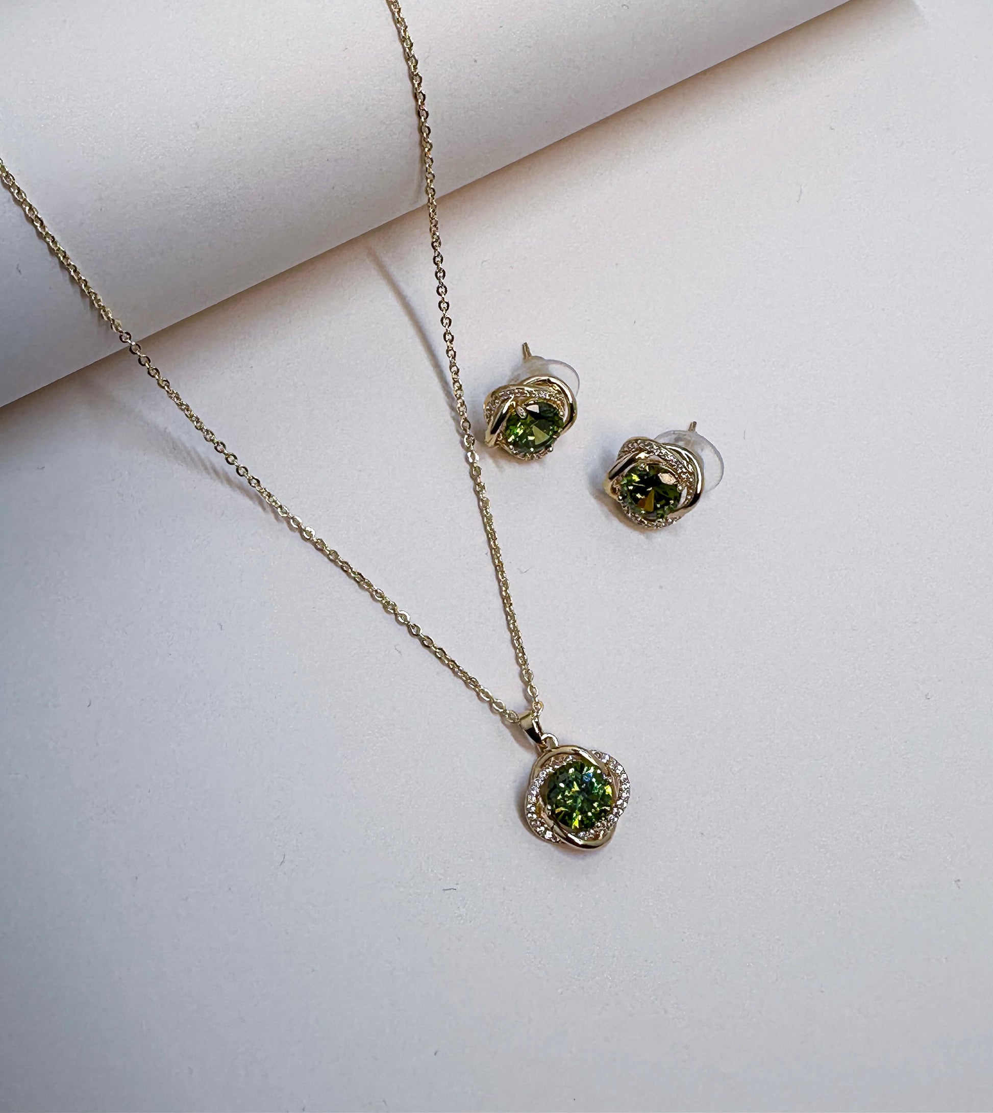 Elara jewelry set displayed on deep green velvet featuring a gold chain necklace with a brilliant deep green central crystal surrounded by a sparkling pave twist frame, and matching stud earrings with deep green stones in Doha Qatar
