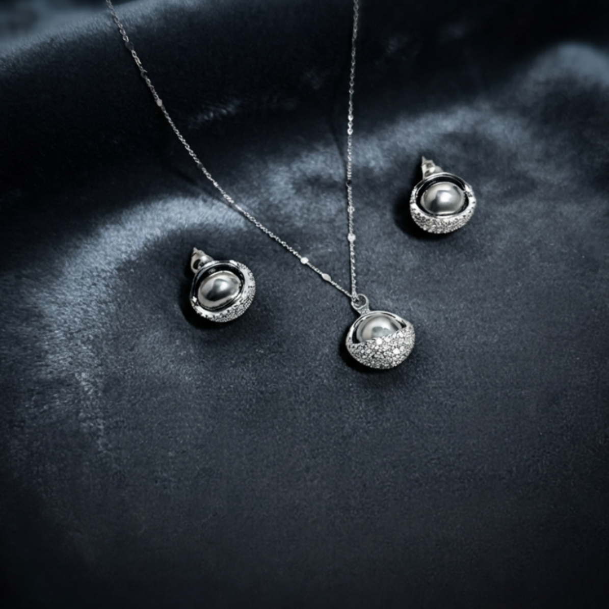Elara jewelry set displayed on deep dark velvet featuring a silver chain necklace with a luminous dark pearl cradled in a sparkling pave-encrusted semi-circle cup, and matching stud earrings with dark pearls and pave details in Doha Qatar
