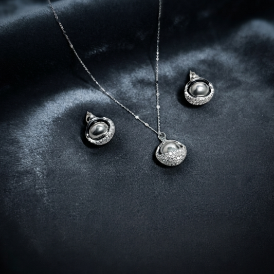 Elara jewelry set displayed on deep dark velvet featuring a silver chain necklace with a luminous dark pearl cradled in a sparkling pave-encrusted semi-circle cup, and matching stud earrings with dark pearls and pave details in Doha Qatar