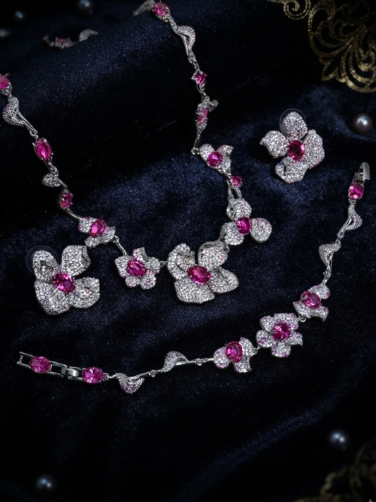 Elara jewelry set displayed on dark velvet featuring a silver-plated floral statement necklace with brilliant fuchsia pink crystal centers and heavy pave-encrusted petals, a matching link bracelet, and coordinating stud earrings in Doha Qatar