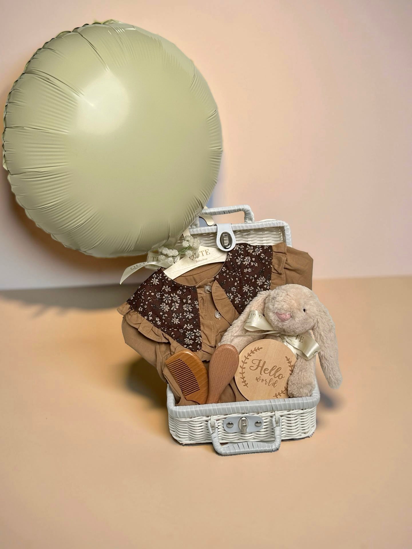 Luxury baby girl gift set in white woven suitcase basket with plush bunny, wooden milestone disc, soft baby outfit, wooden hairbrush set, and balloon by Qute Gifts Doha Qatar