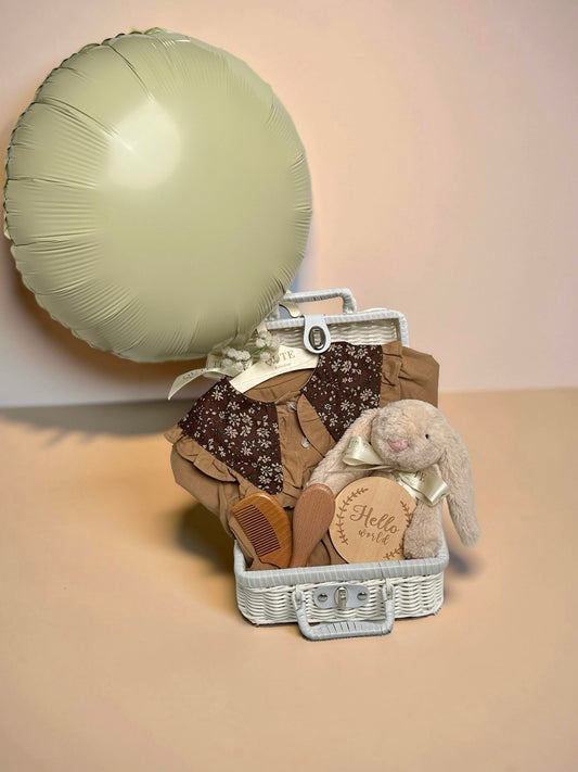 Luxury baby girl gift set in white woven suitcase basket with plush bunny, wooden milestone disc, soft baby outfit, wooden hairbrush set, and balloon by Qute Gifts Doha Qatar