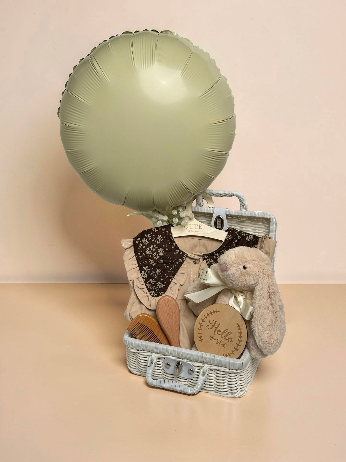 Luxury baby girl gift set in white woven suitcase basket with plush bunny, wooden milestone disc, soft baby outfit, wooden hairbrush set, and balloon by Qute Gifts Doha Qatar