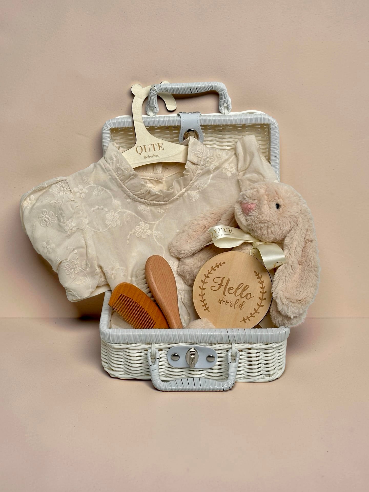Luxury ivory baby girl gift set in white woven suitcase hamper with floral embroidered dress, plush bunny toy, wooden milestone disc, and hairbrush comb set by Qute Gifts Doha Qatar