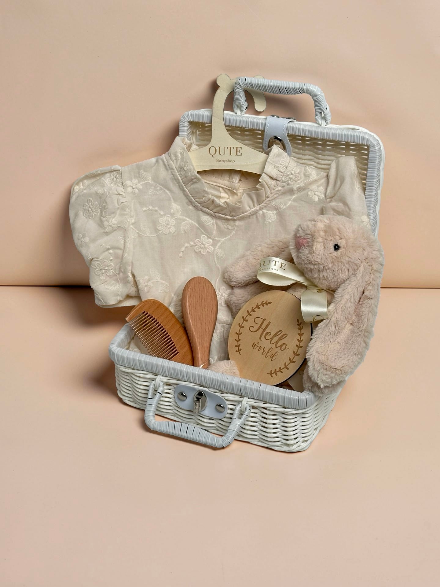 Luxury ivory baby girl gift set in white woven suitcase hamper with floral embroidered dress, plush bunny toy, wooden milestone disc, and hairbrush comb set by Qute Gifts Doha Qatar