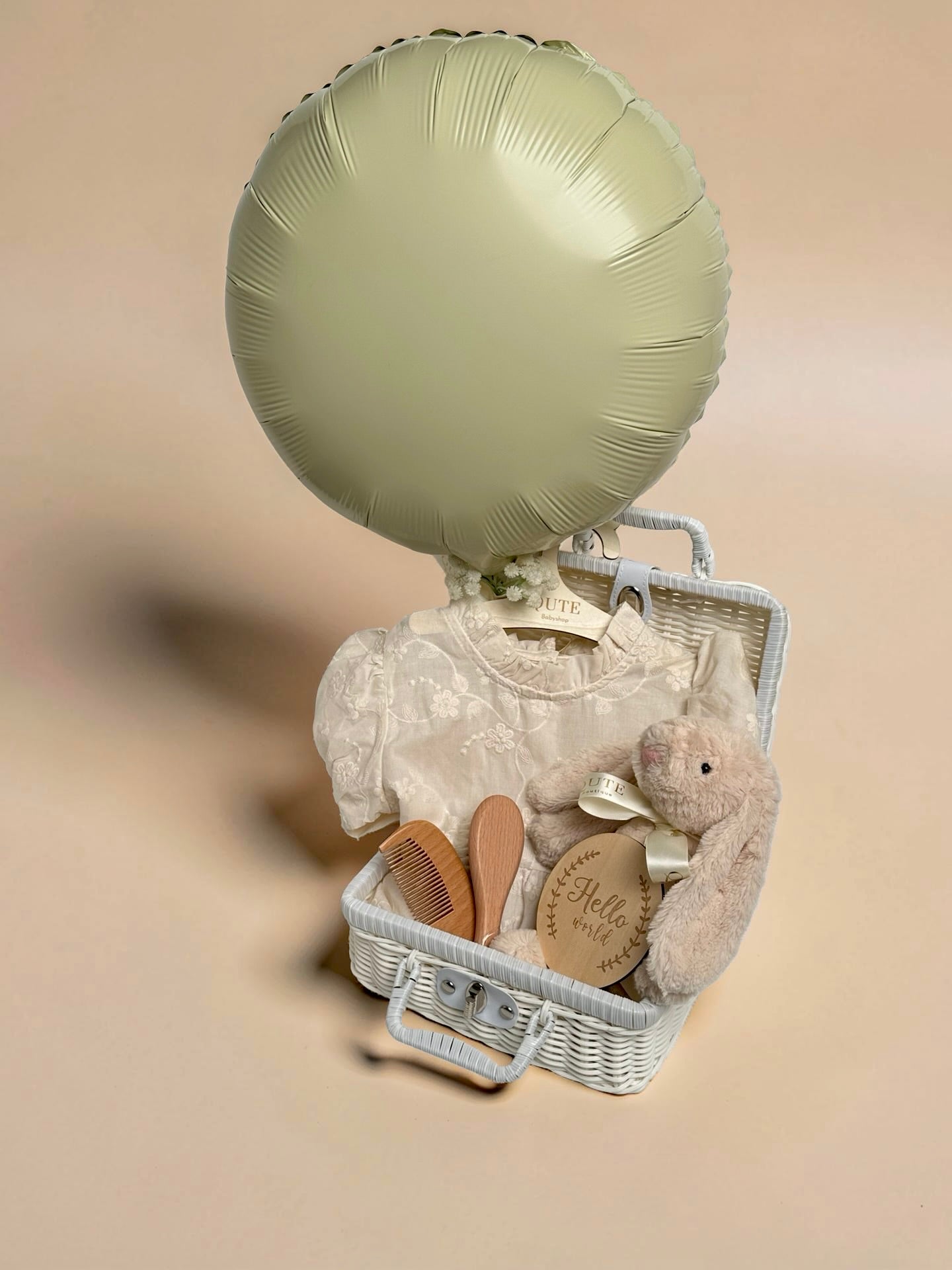 Luxury ivory baby girl gift set in white woven suitcase hamper with floral embroidered dress, plush bunny toy, wooden milestone disc, and hairbrush comb set by Qute Gifts Doha Qatar