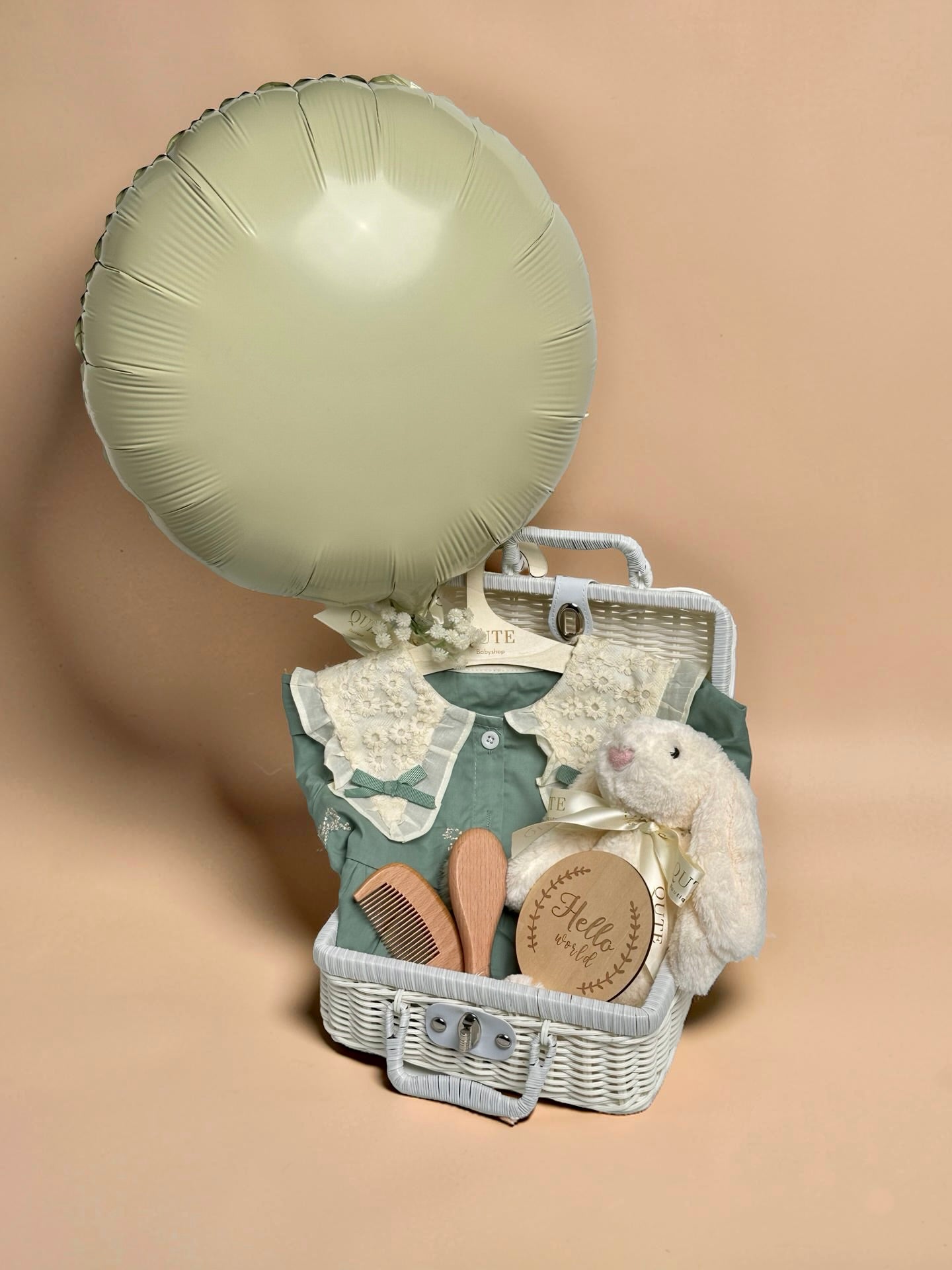 Luxury sage green baby girl gift set in white woven suitcase hamper with lace floral collar dress, plush bunny toy, wooden milestone disc, and hairbrush comb set by Qute Gifts Doha Qatar