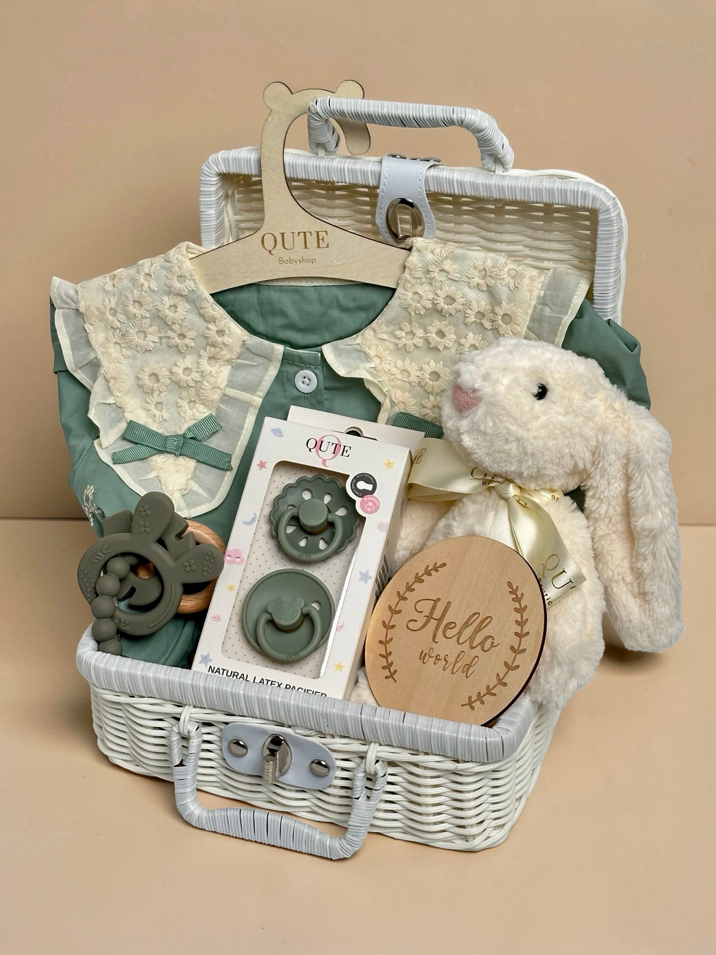 green newborn baby clothing gift setwith white plush bunny toy, pacifiers, teether, and a Hello World milestone card in a white basket—Qute Boutique Gifts 