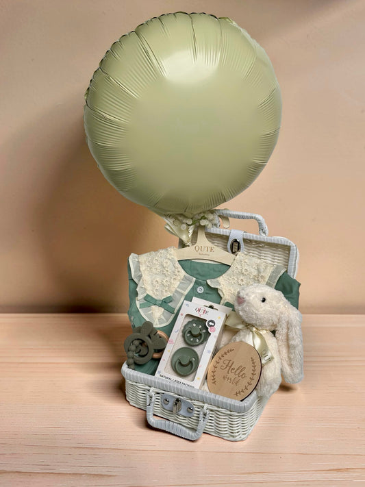 Deluxe sage green baby girl gift set in white woven suitcase hamper with lace collar dress, Qute natural latex pacifiers, silicone teether ring, plush bunny toy, and wooden milestone disc by Qute Gifts Doha Qatar