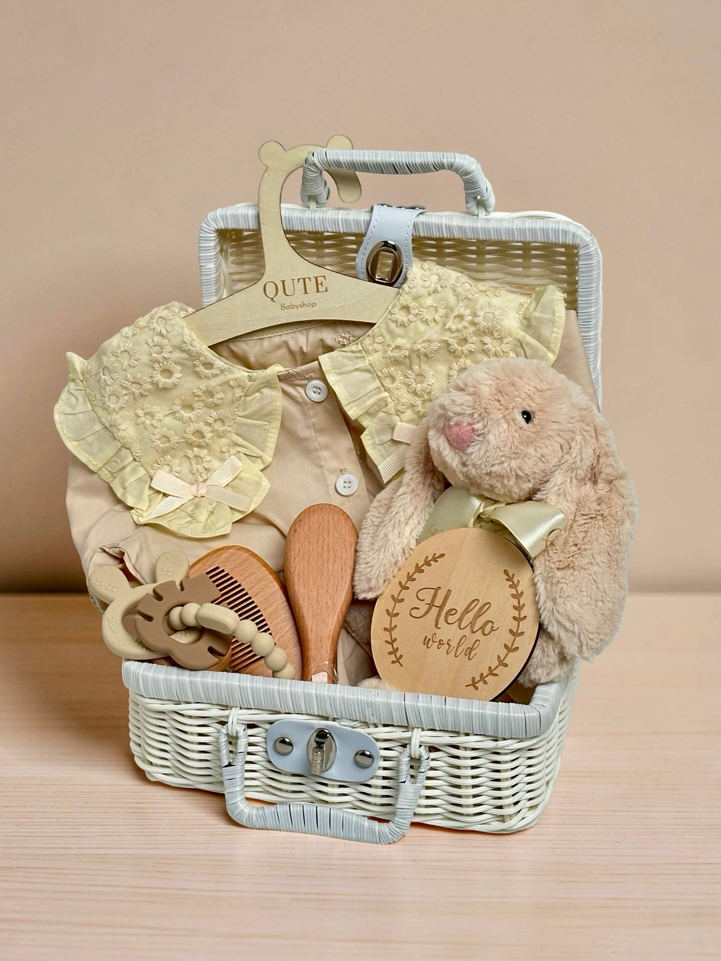 Yellow baby girl gift set in white woven suitcase hamper with floral lace collar dress, plush bunny toy, wooden hairbrush comb set, silicone teether ring, and wooden milestone disc by Qute Gifts Doha Qatar