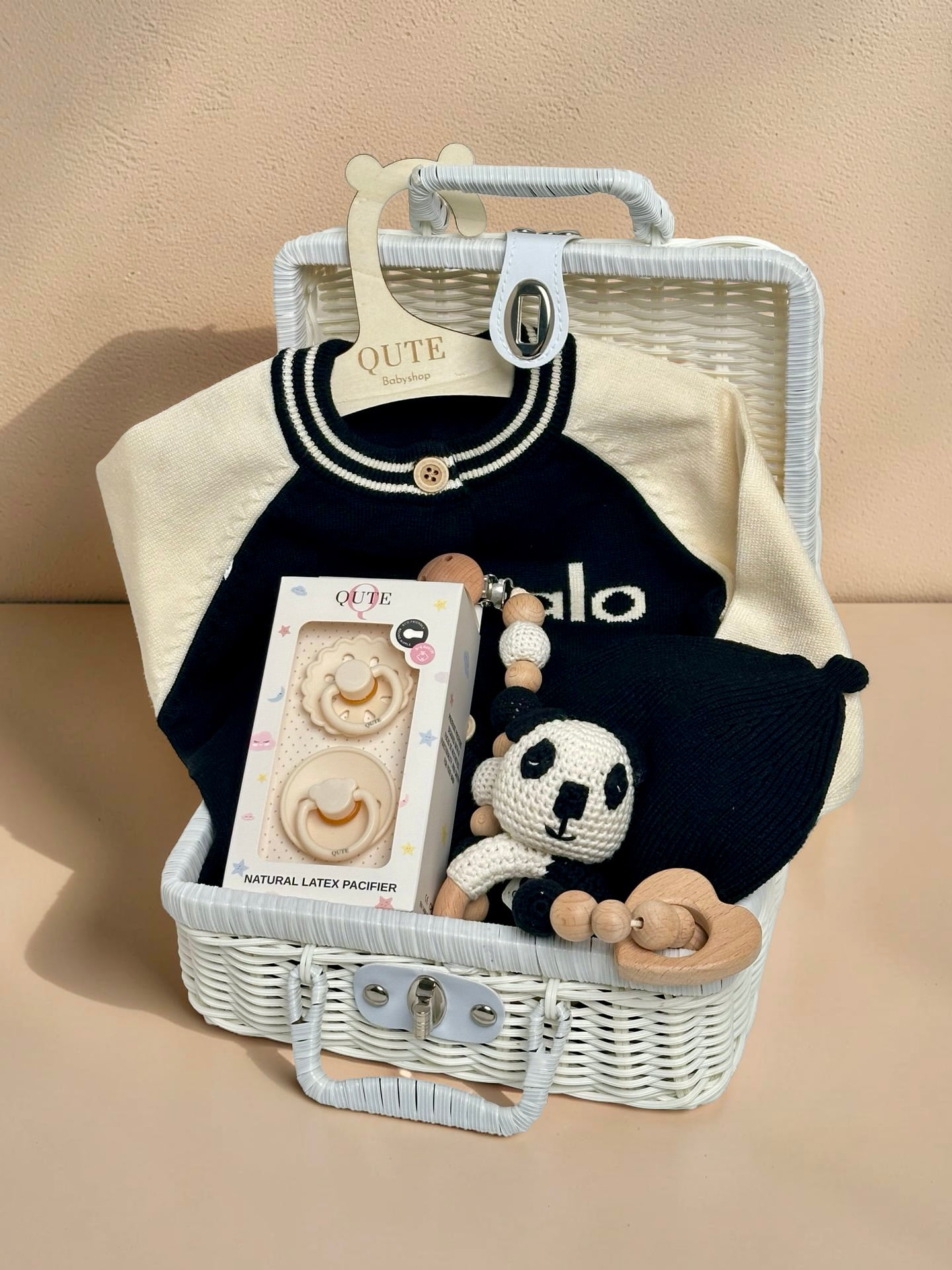 Baby boy gift set in white woven suitcase hamper featuring navy and cream knit cardigan, matching navy beanie, hand-crocheted panda pacifier clip, Qute natural latex pacifiers, and wooden teether by Qute Gifts Doha Qatar