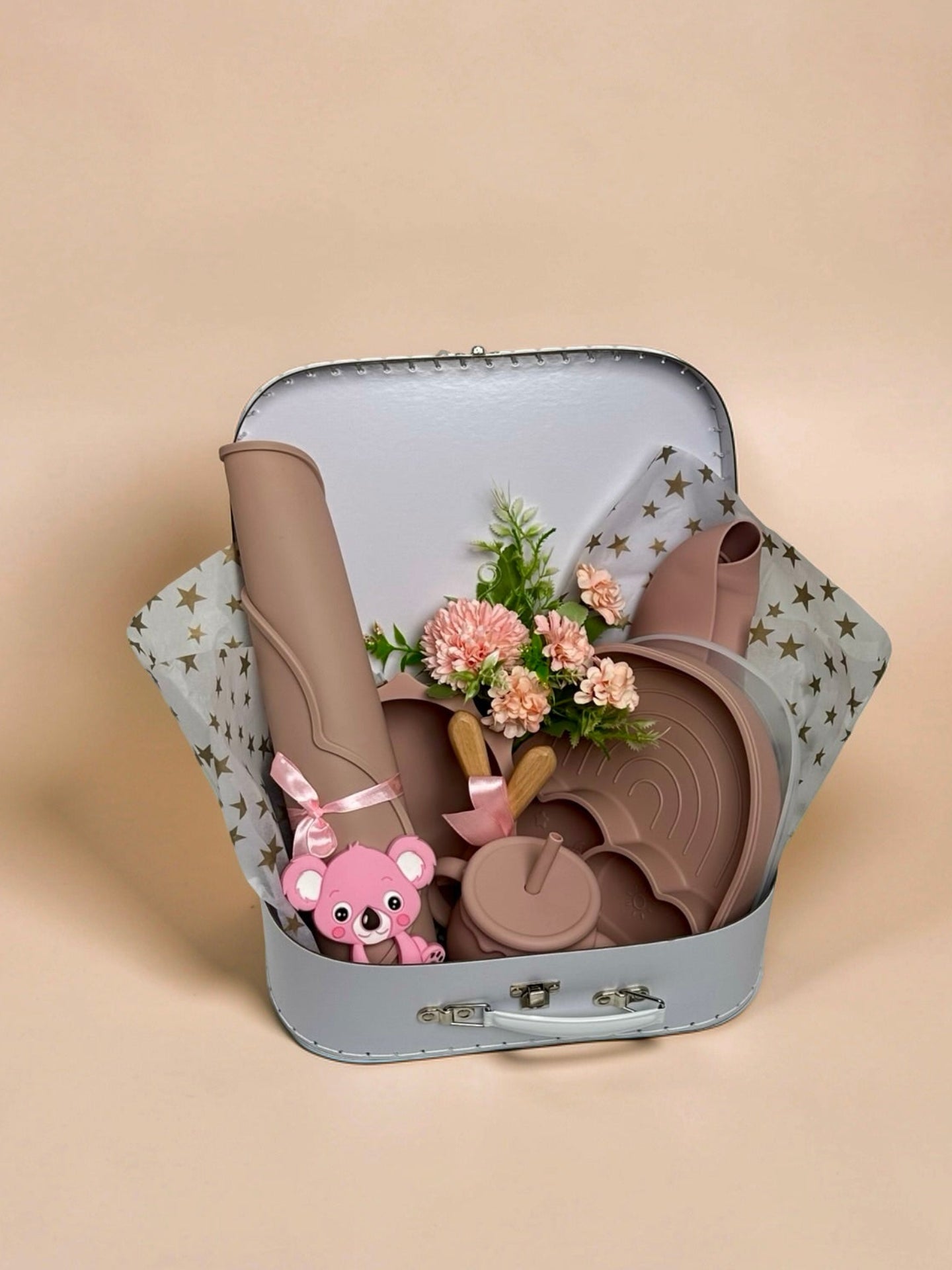 Luxury baby girl toddler weaning and feeding set inside a white keepsake suitcase featuring a divided rainbow silicone plate, large placemat, training cup, silicone bib, pink koala teether, wooden-handled cutlery tied with a pink ribbon, and floral arrangement in Doha Qatar