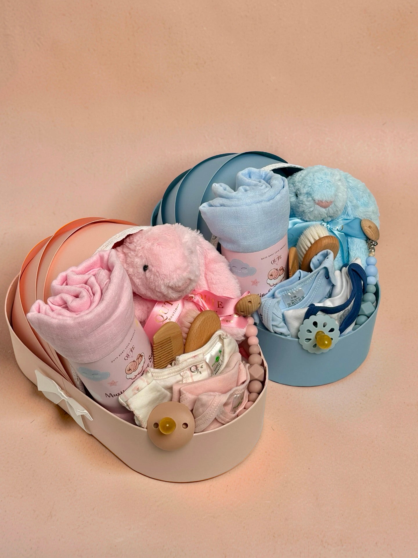 Luxury baby boy and girl newborn gift hamper in a cradle-shaped blue box by Qute Qatar, featuring a blue swaddle, plush bunny, baby clothes, and wooden accessories for delivery in Doha.