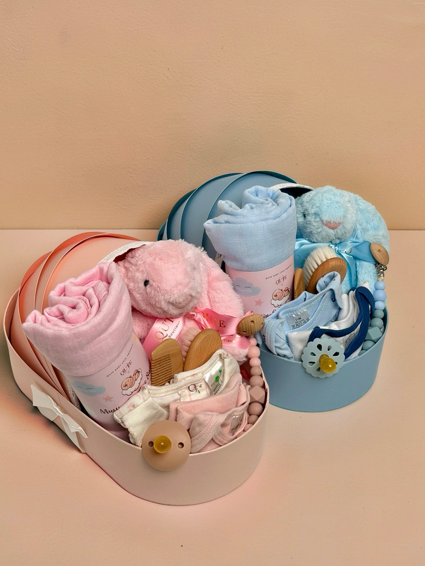 Luxury baby girl newborn gift hamper in a cradle-shaped pink box by Qute Qatar, featuring a pink swaddle, plush bunny, baby clothes, and wooden accessories for delivery in Doha.