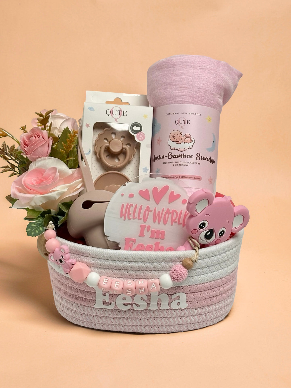 Luxury personalized baby girl gift basket in pink and white woven rope by Qute Qatar, featuring a custom name "Eesha," pink bamboo swaddle, koala teether, pacifier, and floral accents for delivery in Doha.