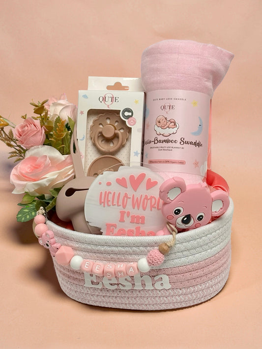 Luxury personalized baby girl gift basket in pink and white woven rope by Qute Qatar, featuring a custom name "Eesha," pink bamboo swaddle, koala teether, pacifier, and floral accents for delivery in Doha.