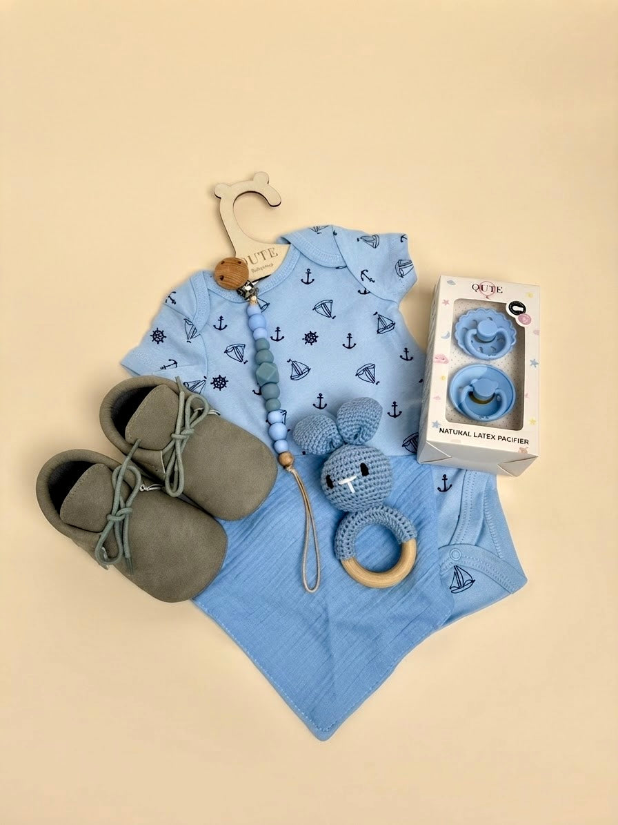 Luxury baby boy newborn gift set in a white keepsake suitcase by Qute Qatar, featuring a 1-3 months nautical bodysuit, moccasins, natural latex pacifiers, and a crocheted bunny for delivery in Doha.
