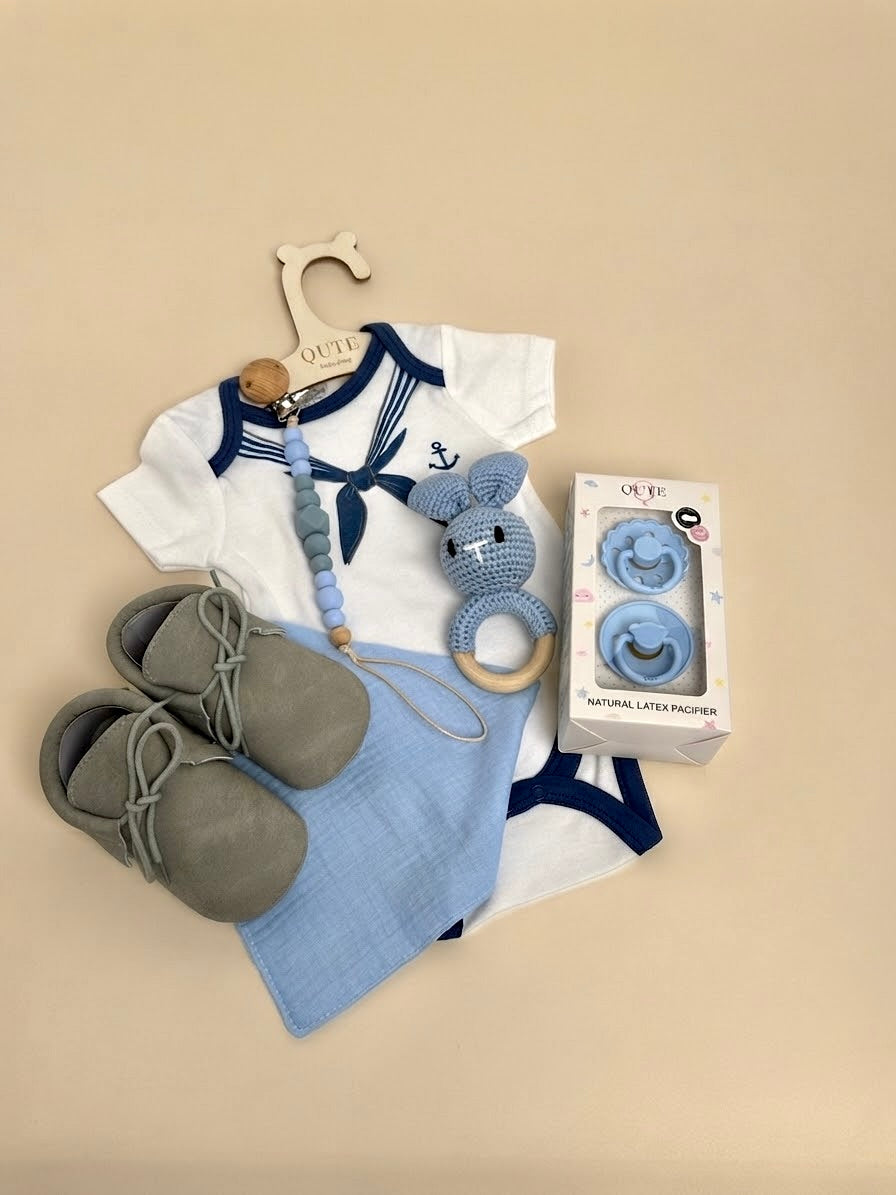 Luxury baby boy newborn gift set in a white keepsake suitcase by Qute Qatar, featuring a 1-3 months marine-collar bodysuit, moccasins, natural latex pacifiers, and a crocheted bunny for delivery in Doha.