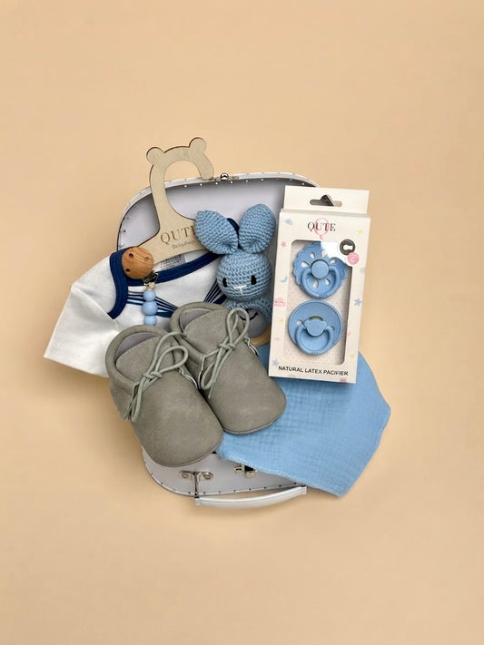 Luxury baby boy newborn gift set in a white keepsake suitcase by Qute Qatar, featuring a 1-3 months marine-collar bodysuit, moccasins, natural latex pacifiers, and a crocheted bunny for delivery in Doha.