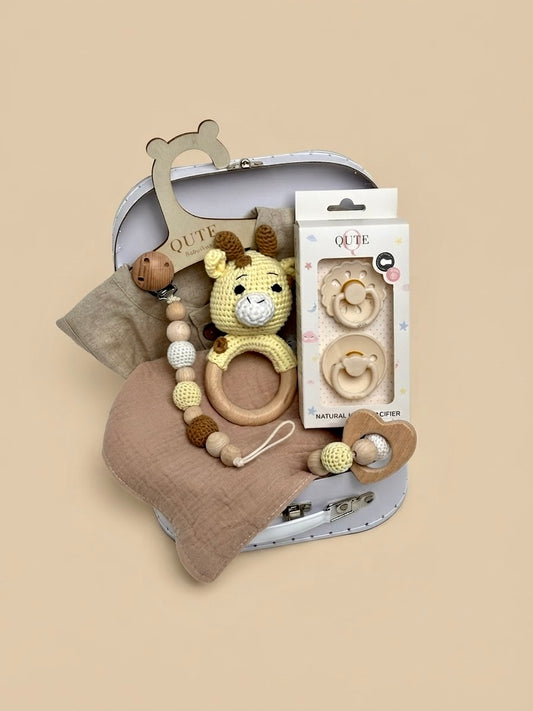Luxury newborn baby gift set in a white keepsake suitcase by Qute Qatar, featuring a 1-3 months neutral linen-style outfit, giraffe rattle, natural latex pacifiers, and wooden accessories for delivery in Doha.