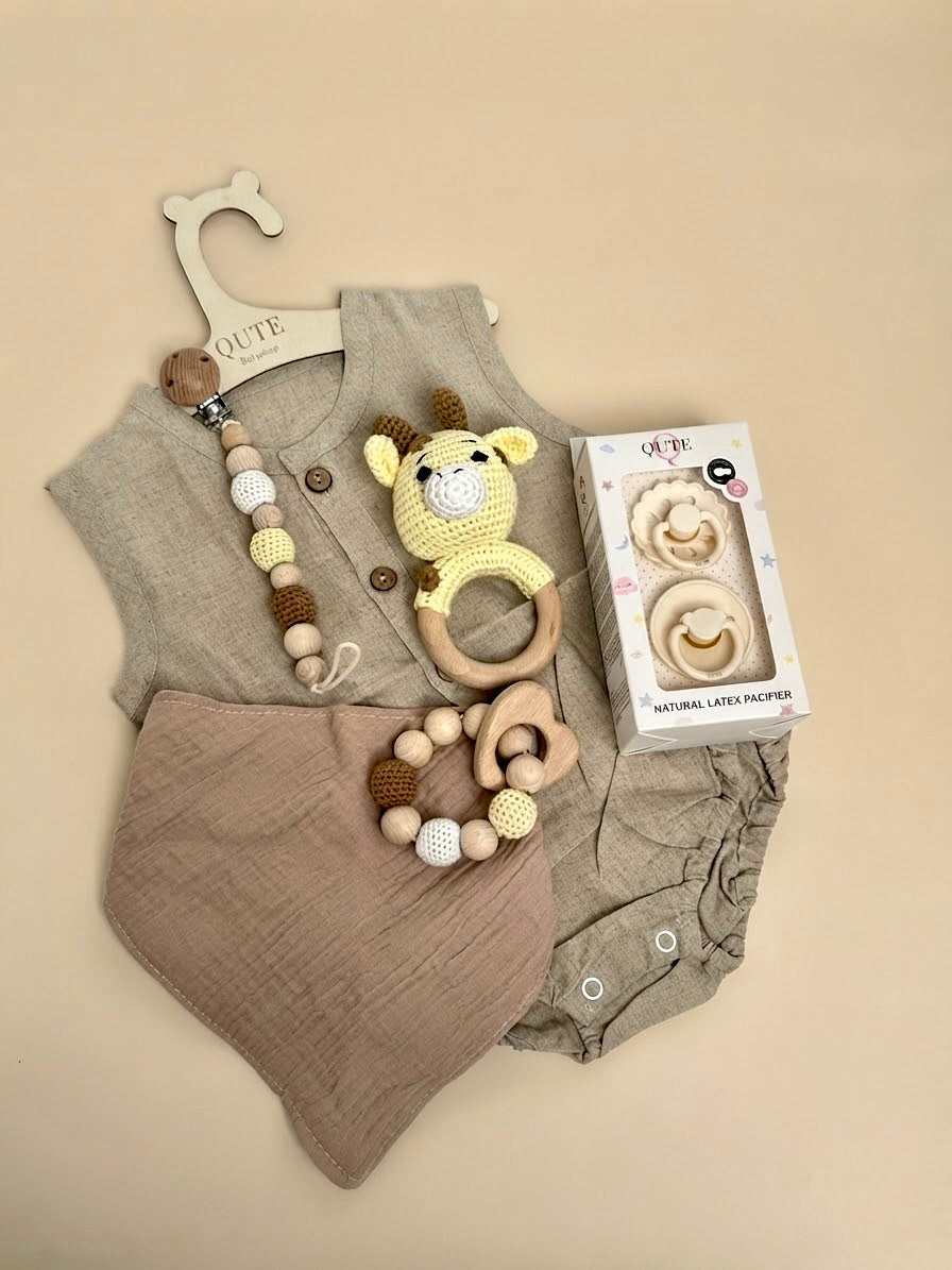Luxury newborn baby gift set in a white keepsake suitcase by Qute Qatar, featuring a 1-3 months neutral linen-style outfit, giraffe rattle, natural latex pacifiers, and wooden accessories for delivery in Doha.