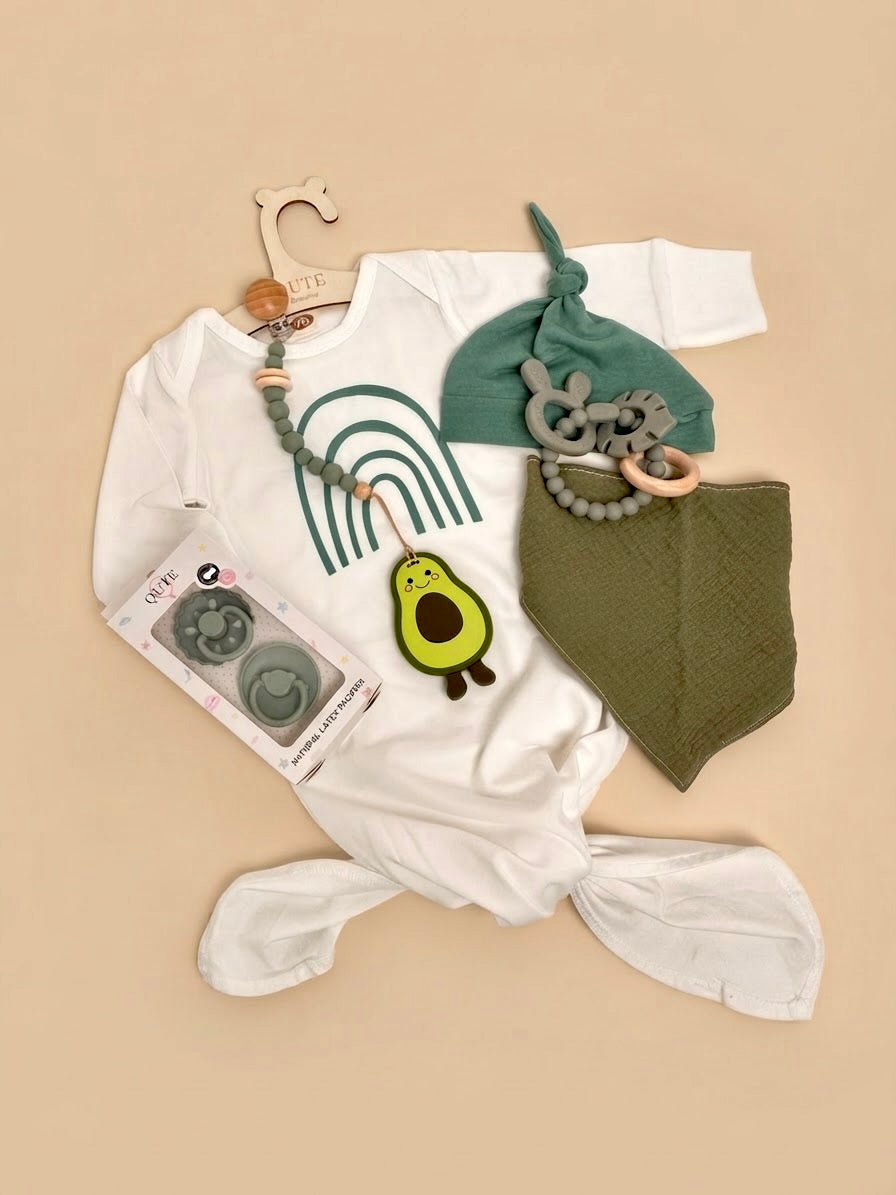 Luxury newborn baby gift set in a white keepsake suitcase by Qute Qatar, featuring a 3-6 months sage green outfit, avocado teether, pacifiers, and teething accessories for delivery in Doha.