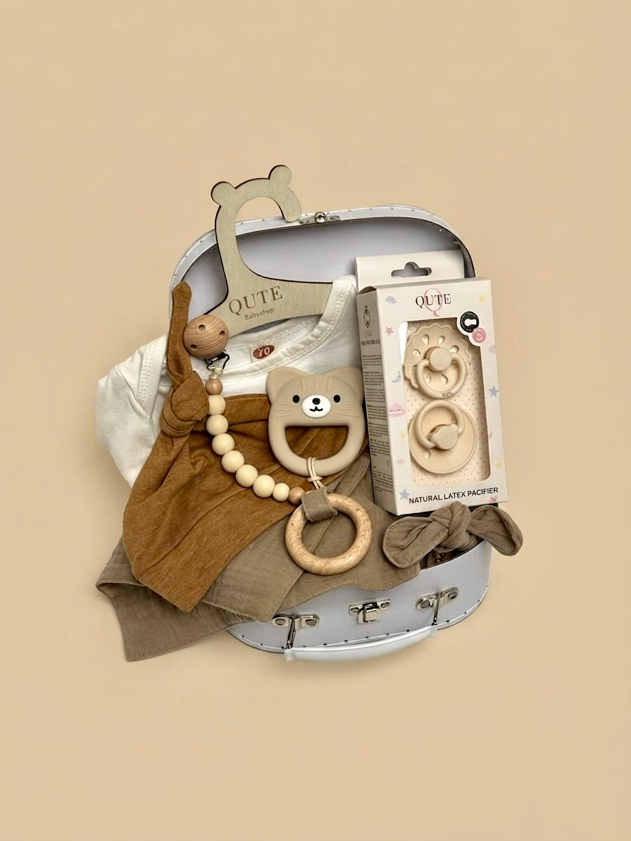 Luxury newborn baby gift set in a white keepsake suitcase by Qute Qatar, featuring a 3-6 months caramel outfit, bear teether, natural latex pacifiers, and wooden accessories for delivery in Doha.