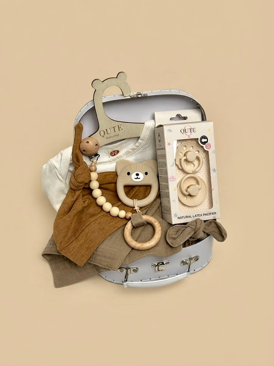 Luxury newborn baby gift set in a white keepsake suitcase by Qute Qatar, featuring a 3-6 months caramel outfit, bear teether, natural latex pacifiers, and wooden accessories for delivery in Doha.