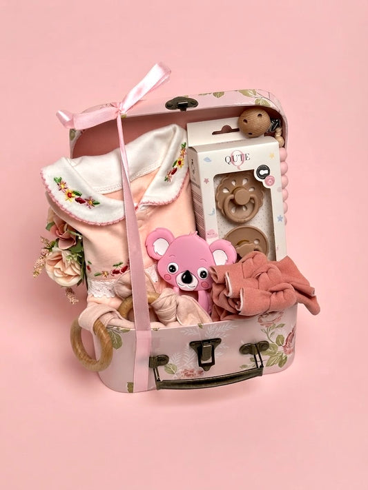 Luxury baby girl newborn gift set in a floral keepsake suitcase by Qute Qatar, featuring a 3-6 months full-leg romper, koala teether, pacifiers, and wooden accessories for delivery in Doha.
