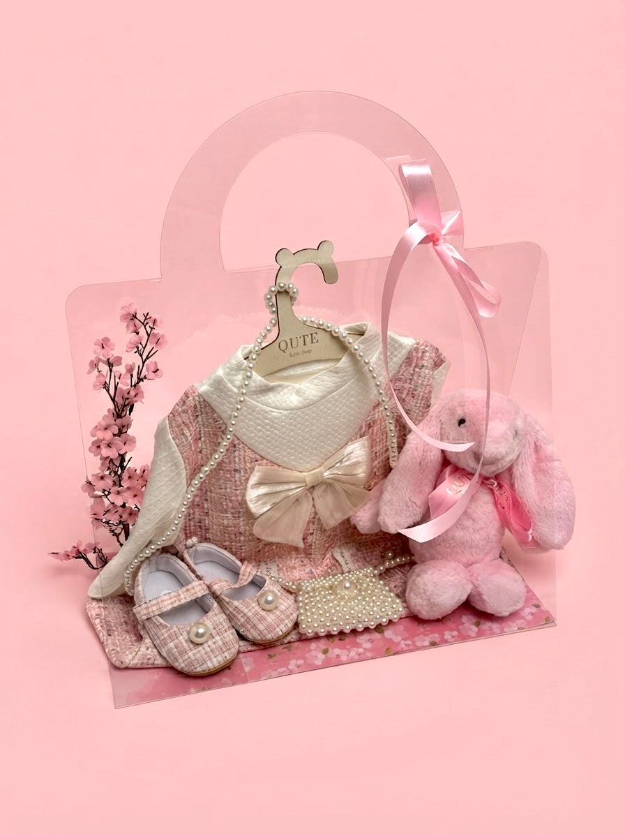 Luxury baby girl gift set for 12-18 months in a clear presentation bag by Qute Qatar, featuring a pink tweed dress, matching shoes, pearl mini bag, and a plush pink bunny for delivery in Doha.