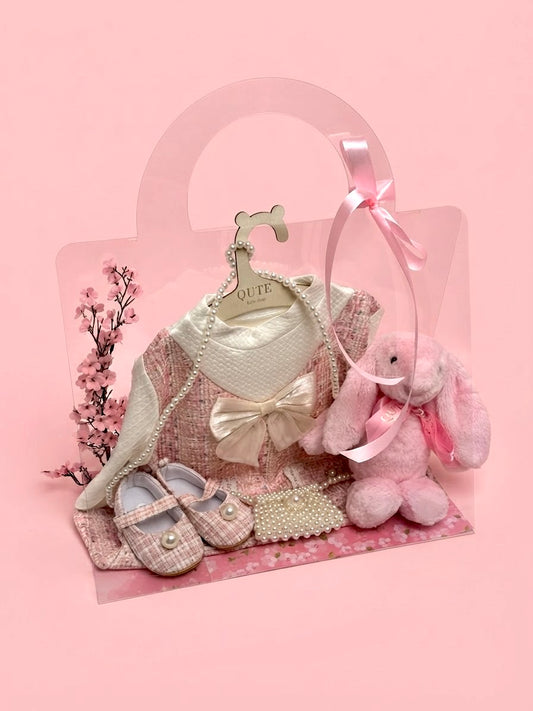 Luxury baby girl gift set for 12-18 months in a clear presentation bag by Qute Qatar, featuring a pink tweed dress, matching shoes, pearl mini bag, and a plush pink bunny for delivery in Doha.