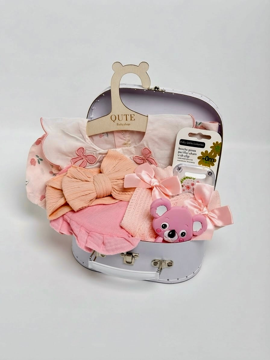 Luxury baby girl newborn gift set in a white keepsake suitcase by Qute Qatar, featuring a 3-6 months pink floral outfit, koala teether, hair bows, and accessories for delivery in Doha.