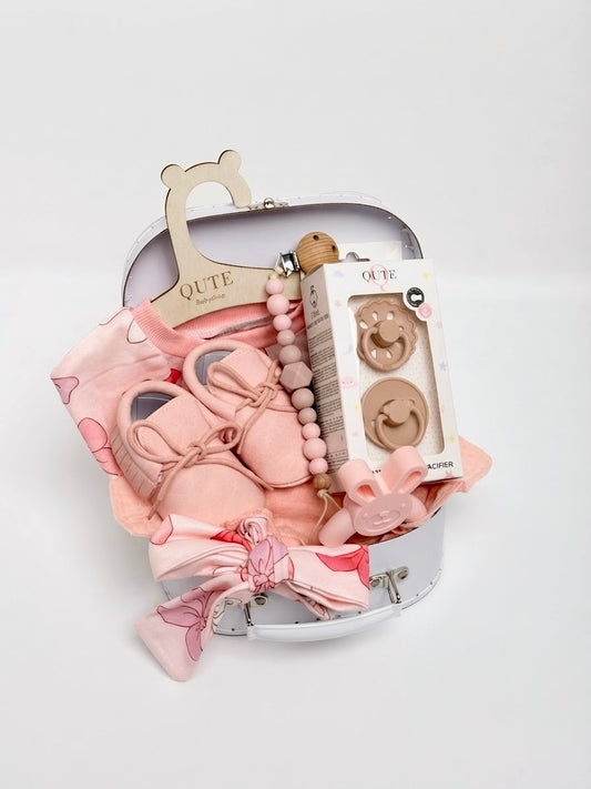 Luxury baby girl newborn gift set in a keepsake box by Qute Qatar, featuring a 3-6 months pink bow-print outfit, ruffled bib, bunny teether, soft shoes, and natural latex pacifiers for delivery in Doha.