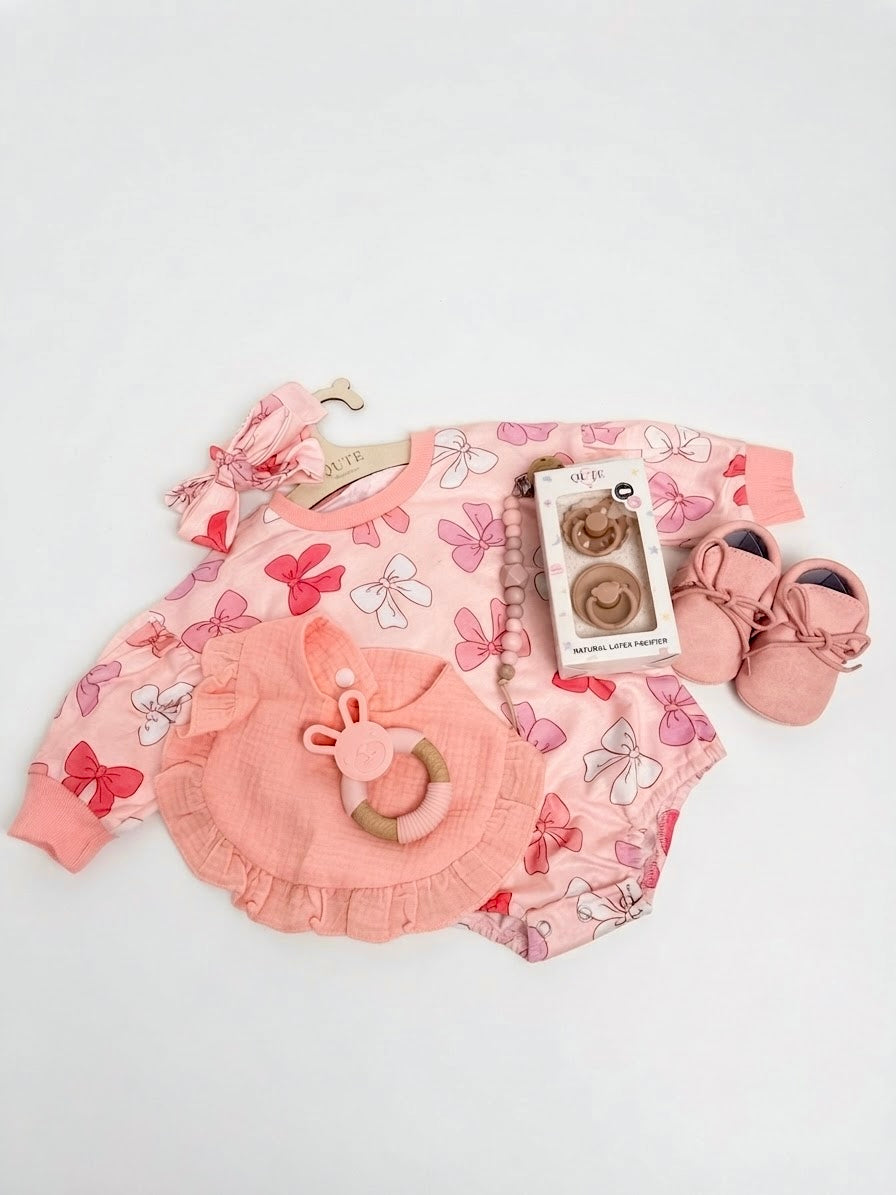 Luxury baby girl newborn gift set in a keepsake box by Qute Qatar, featuring a 3-6 months pink bow-print outfit, ruffled bib, bunny teether, soft shoes, and natural latex pacifiers for delivery in Doha.