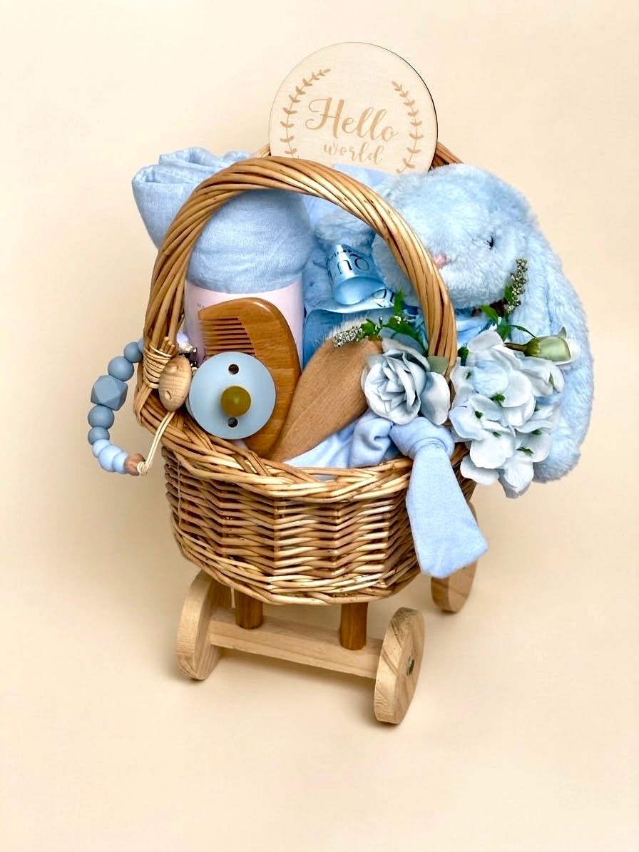 Luxury newborn baby boy gift set in a wheeled wooden carriage basket by Qute Qatar, featuring a bamboo swaddle, plush bunny, milestone disc, and floral accents for delivery in Doha.