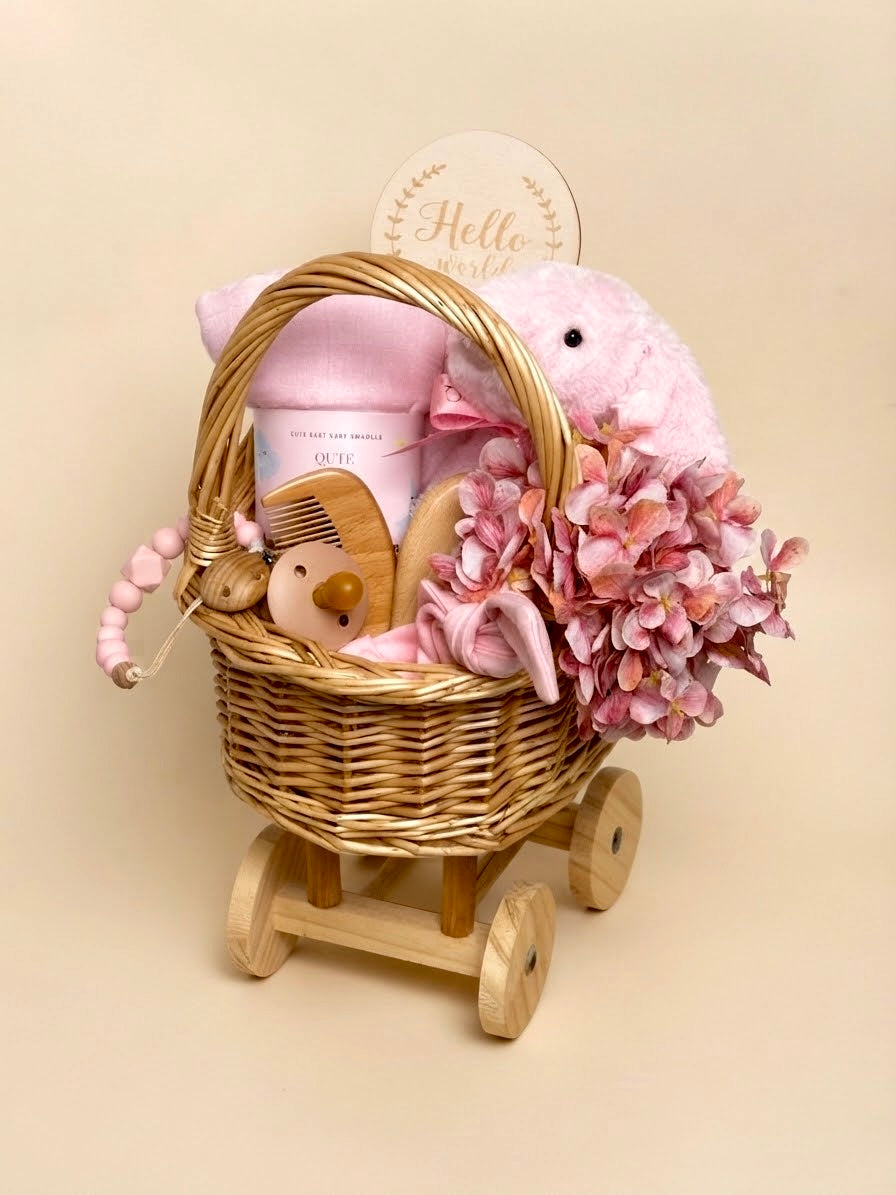 Luxury newborn baby girl gift set in a wheeled wooden carriage basket by Qute Qatar, featuring a pink bamboo swaddle, plush bunny, milestone disc, and floral accents for delivery in Doha.  
