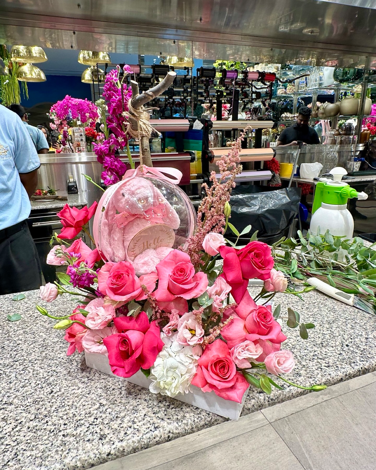 Baby Bloom Bubble newborn flower arrangement featuring pink roses, stock flowers, and an acrylic bubble with a pink plush toy and "Hello Little One" tag.   
