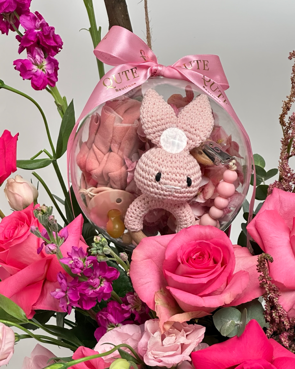 Baby Bloom Bubble newborn flower arrangement featuring pink roses, stock, and an acrylic keepsake bubble containing a handmade pink crochet bunny.   