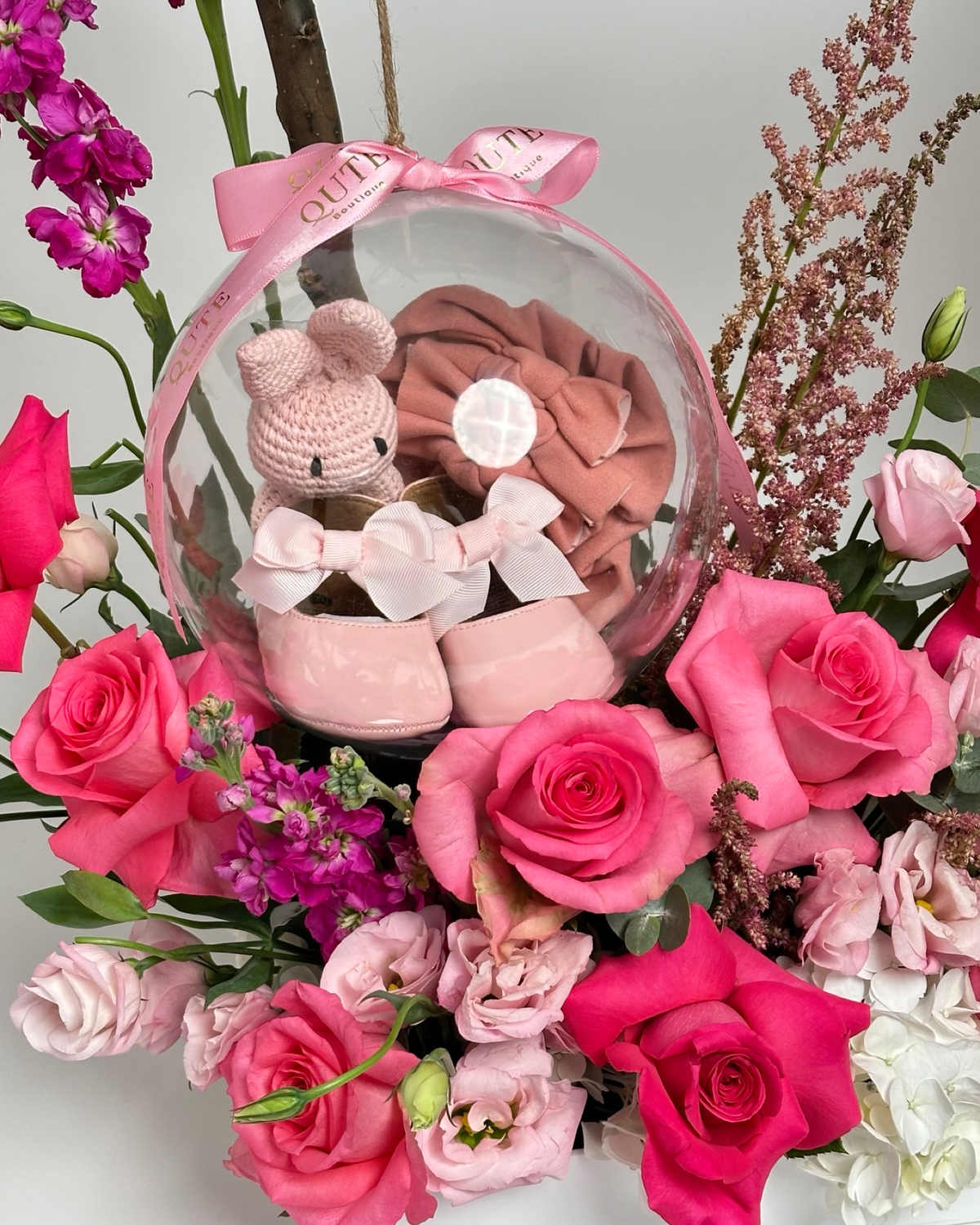 Same-day baby girl gift box featuring luxury pink roses and an acrylic keepsake bubble with baby booties and hair accessories for welcoming a newborn.   